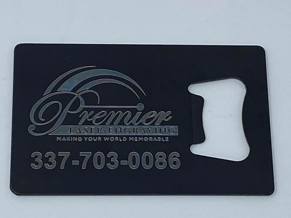 Black Metal Bottle Opener Shaped like a Business Card, engraved with the Premier Laser Engraving Logo and phone number 337-703-0086